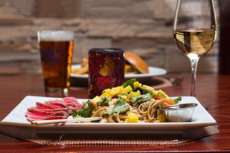 Plated entree with noodles, steak and vegetables with a glass of white wine